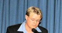 Blonder Mann im Sakko mit Brille spricht in ein Mikrofon vor blauem Vorhang, Quelle: DTF