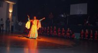 Tänzerin in bunter Kleidung mit Schleier vor einer Reihe junger Tänzerinnen in roten Kleidern, Quelle: DTF