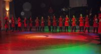 Reihe junger Tänzerinnen in roten Kleidern auf bunt beleuchteter Tanzfläche, Quelle: DTF