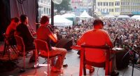 Band sitz auf der Bühne mit Publikum im Bildhintergrund, Quelle: DTF