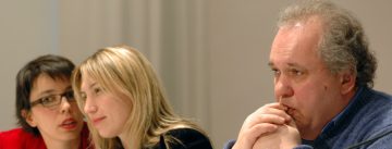 zwei Frauen und ein Mann sitzen an einem langen Tisch mit Namensschildern vor sich