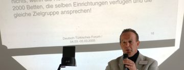 Mann im grauen Anzug steht sprechend an einem OHP