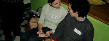 zwei Frauen sitzen eng beieinander, die eine hat ein Kochbuch auf dem Schoß