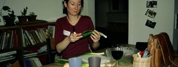 Frau sitzt an einem Tisch und hält Stange Lauch in der Hand