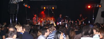 Band auf rot beleuchteter Bühne vor Publikum