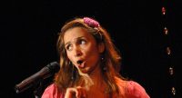 Frau in pinkem Oberteil spricht gestikulierend auf der Bühne, Quelle: DTF