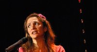 Frau in pinkem Oberteil spricht gestikulierend auf der Bühne, Quelle: DTF