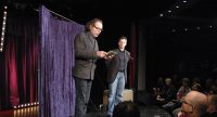 Mann und Kerim Arpad sprechen auf der Bühne vor einem violetten Vorhang, Quelle: DTF