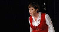 Frau im roten Kleid spricht auf der Bühne vor Silhouette des Publikums, Quelle: DTF