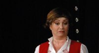 Frau im roten Kleid spricht auf der Bühne vor Silhouette des Publikums, Quelle: DTF