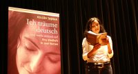 Nilgün Tasman liest aus ihrem Buch vor Banner mit dem Buchcover, Quelle: DTF