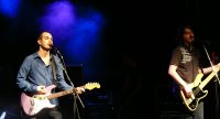 Sänger/Gitarrist und Bassist nebeneinander auf blau beleuchteter Bühne, Quelle: DTF