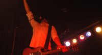 Gitarrist/Sänger auf rot beleuchteter Bühne reckt die rechte Hand in die Luft, Quelle: DTF