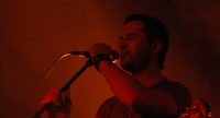 Gitarrist/Sänger auf rot beleuchteter Bühne greift das Mikrofon mit beiden Händen, Quelle: DTF