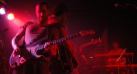 Gitarristen lehnend spielend aneinander auf rot beleuchteter Bühne, Quelle: DTF