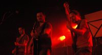 Gitarristen und Bassist nebeneinander auf rot beleuchteter Bühne, Quelle: DTF