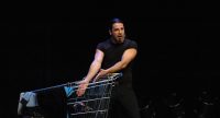 Bülent Ceylan schiebt einen Einkaufswagen über die Bühne vor Silhouette des Publikums, Quelle: DTF