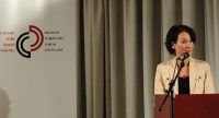 Frau im beigen Sakko am Rednerpult, Quelle: DTF