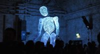 Dunkler Saal mit blauer Riesenfigur, Quelle: DTF
