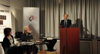 Diskussionteilnehmer*innen, neben ihnen spricht ein Mann am Rednerpult, Quelle: DTF