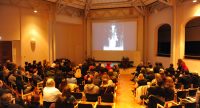 Menschen im Publikum schauen auf Bilder-Slideshow auf der Bühne, Quelle: DTF