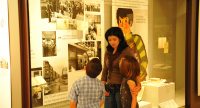 Frau mit zwei Kindern vor einer Ausstellungsvitrine, Quelle: DTF