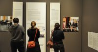 Menschen im Ausstellungsraum schauen sich ausgestellte Wände mit Text und Bilder an, Quelle: DTF