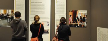 Menschen im Ausstellungsraum schauen sich ausgestellte Wände mit Text und Bilder an