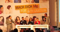 Menschen sitzend an einem Holztisch vor Silhouette des Publikums, Quelle: DTF