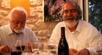 zwei ältere Herren sitzen an einem gedeckten Tisch, der eine lacht in die Kamera, Quelle: DTF