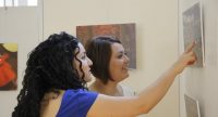 zwei Frauen in einem Ausstellungsraum, die eine zeigt mit dem rechten Zeigefinger auf ein Bild, Quelle: DTF