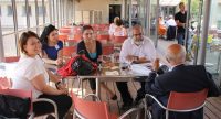 drei Frauen und zwei Männer sitzen an einem Tisch im Glassaal eines Restaurants und unterhalten sich, Quelle: DTF