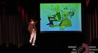 Mann zeigt auf die Projektion einer Karikatur vor Silhouette des Publikums, Quelle: DTF