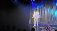 Mann im weißen ANzug auf blau beleuchteter Bühne vor Silhouette des Publikums, Quelle: DTF