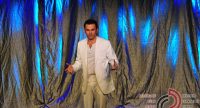 Mann im weißen Anzug auf blau beleuchteter Bühne, Quelle: DTF