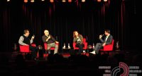 Diskussionsteilnehmer sitzend auf der Bühne auf roten Sesseln vor Silhouette des Publikums, Quelle: DTF