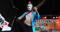 Mann mit schwarz-weißer Maske im blauen Mantel spielt traditionelles Saiteninstrument, Quelle: DTF