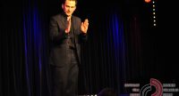 Mann im schwarzen Anzug spricht gestikulierend auf der Bühne vor Silhouette des Publikums, Quelle: DTF