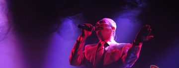 Mann im weißen Anzug singt auf violett beleuchteter Bühne
