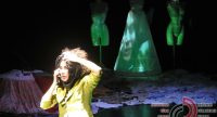 Frau in gelb-grünem Sakko fasst sich an den Kopf, hinter ihr stehen grün beleuchtete Mannequins, Quelle: DTF