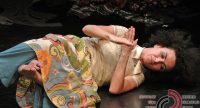 Frau mit buntem Kleid liegt mit geschlossenen Augen und gekreuzten Armen auf dem Boden, Quelle: DTF