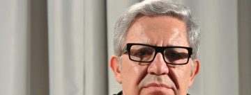 Autor stützt sich das Kinn mit der rechten Hand und schaut in die Kamera