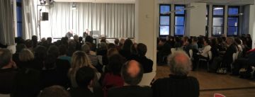 Publikum sitzend schaut Menschen auf dem Podium zu