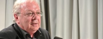 Mann im schwarzen Sakko spricht Richtung Publikum