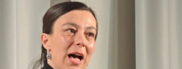 Frau im schwarzen Rollkragenpullover spricht ins Mikrofon