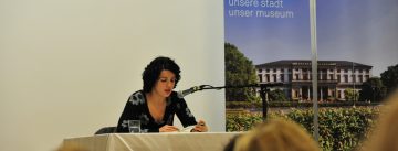 Dilek Güngör sitzt an einem weißen Tisch neben Banner des Stadtmuseums