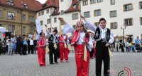 Mädchen und Jungs in traditioneller Kleidung stehen auf dem Platz mit schräg erhobener rechter Hand und linker Hand an der Hüfte, Quelle: DTF