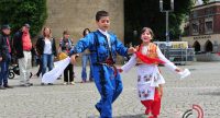 Mädchen und Junge in traditioneller Kleidung tanzend mit kleiner Menschengruppe im HIntergrund, welche die beiden boebachtet, Quelle: DTF