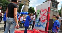 Kinder in blauen Shirts malen auf eine Leinwand während ihnen eine Frau in gebleichten Jeans zuschaut, Quelle: DTF