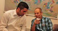 zwei sprechende Männer sitzen nebeneinander mit Kafeebechern in den Händen, Quelle: DTF